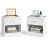 Two white nightstands are shown against a white background. The nightstands have drawers and open shelves. The left nightstand has a framed picture on top, and books inside the shelf. The right nightstand has a desk calendar and a small plant on top, and b Produktbild-Vorschau