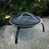 A black portable fireplace with a grill grate and a poker, set on a gravel surface with greenery in the background. Náhľad obrázku produktu