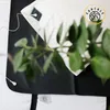 A close-up shot of a white pillow with a green plant branch in front of it, placed on a black surface. Produktbild-Vorschau