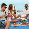 Three people are sitting on a blue blanket on the beach, with pizza and drinks. Produktbild-Vorschau