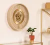 A beige and gold mechanical wall clock with Roman numerals is displayed on a white wall. Voir les images du produit