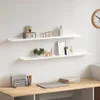Two white wall shelves are mounted on a white wall above a wooden desk. The shelves are decorated with various items, including decorative objects, a plant, and picture frames. The desk has a document holder, pens, a laptop, and books. Náhľad obrázku produktu