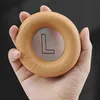 A hand holds a tan-colored ear pad with an 'L' logo on it. Produktbild-Vorschau