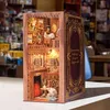A 3D DIY book nook kit designed to look like a miniature library or room, placed on a white surface with a blurred background of bookshelves. Voir les images du produit