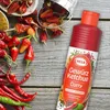 A bottle of Hela Gewürz Ketchup Curry is placed on a wooden surface surrounded by various chili peppers and spices. Produktbild-Vorschau