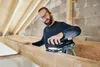 A man is sanding a wooden beam in an attic or unfinished room. Voir les images du produit