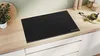 A modern kitchen countertop with a black induction hob, a plant, and kitchen utensils. Náhľad obrázku produktu