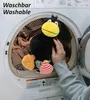 A person's hand is placing a stuffed crow toy into a washing machine. Produktbild-Vorschau