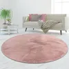 A round pink rug is placed on a light-colored floor in front of a sofa with pillows and a blanket. Produktbild-Vorschau