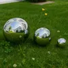 Three polished stainless steel garden spheres of different sizes are placed on a green lawn with some small yellow flowers and green plants. Produktbild-Vorschau