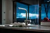 A modern kitchen sink with a faucet, set against a large window with a dramatic twilight sky and landscape view. Decorative bottles and a bowl of apples are on the counter. Podgląd zdjęcia produktu