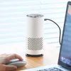 A white cylindrical air purifier is placed on a wooden desk next to a laptop and a computer mouse. A hand is visible operating the mouse. Produktbild-Vorschau