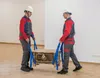 Two people are using lifting straps to move a chest. Produktbild-Vorschau