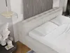 A close-up view of a beige upholstered bed with white bedding and pillows, set against a textured wall. Produktbild-Vorschau