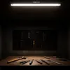 A workbench with tools displayed on a pegboard and on the table, illuminated by a long fluorescent light. Náhľad obrázku produktu
