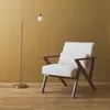 A cream-colored armchair with wooden legs and a floor lamp with a gold finish stand against a mustard-yellow wall. Anteprima dell’immagine prodotto