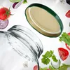 A glass jar with a green lid and various salad ingredients floating around it. Podgląd zdjęcia produktu