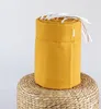 A rolled-up yellow baby bed bumper on a woven stool. Produktbild-Vorschau