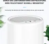 A close-up view of the top of a white dehumidifier with a perforated grill, surrounded by green leaves. Produktbild-Vorschau