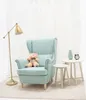 A teddy bear sits on a light blue armchair next to two small side tables, a floor lamp, and a curtain in the background. Podgląd zdjęcia produktu