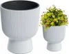 Two white planters on a white background. One planter is empty and the other contains a green plant with pink flowers. Produktbild-Vorschau