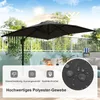 An outdoor patio scene with a large black umbrella providing shade over a table. The background shows a balcony railing, trees, and a blue sky with sun rays. Podgląd zdjęcia produktu