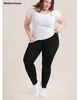 Plus-Size-Frau, die schwarze Leggings, ein weißes T-Shirt und weiße Sneakers trägt, lächelnd Náhled obrázku produktu