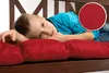A young boy is lying on a red cushion on a wooden bench. Produktbild-Vorschau