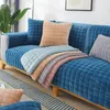 Blauer gesteppter Samt-Sofabezug auf einem Sofa, mit einem Stapel mehrfarbiger Bezüge und einem pfirsichfarbenen Kissen Náhľad obrázku produktu