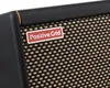 A close-up view of a guitar amplifier speaker grille with a brand logo. Náhled obrázku produktu