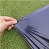 Hand, die eine schwarze Plastikfolie gegen einen grünen grasigen Hintergrund hochhält Anteprima dell’immagine prodotto