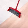 A red and gray broom is shown sweeping across a floor that transitions from light gray tiles to light wood. Anteprima dell’immagine prodotto