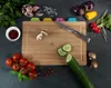 A collection of fresh vegetables and herbs arranged around a wooden cutting board with a knife and sliced vegetables on it. Anteprima dell’immagine prodotto