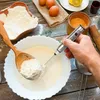 A hand is using a silver electric frother to mix batter in a white bowl, with a wooden spoon holding flour nearby. Produktbild-Vorschau