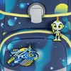 A close-up view of a blue backpack with a space-themed pattern, featuring a gray buckle and two attached charms: a robot and a spaceship. Podgląd zdjęcia produktu