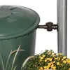 A close-up of a green rain barrel with a brown spigot attached to a metal pole, with yellow flowers and grass in the foreground. Náhled obrázku produktu