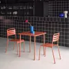A terracotta table and two chairs set against a black tiled wall. Produktbild-Vorschau