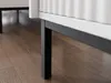 A close-up shot of the legs and bottom edge of a white cabinet with a black frame, resting on a wooden floor. Náhled obrázku produktu