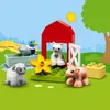 A farm scene with LEGO DUPLO figures of a duck, pig, sheep, and cat, along with a red barn, yellow hay bales, and a yellow flower. Podgląd zdjęcia produktu