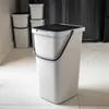 A gray plastic trash can with a black lid and handle sits on a marble floor in front of a dark appliance. Produktbild-Vorschau