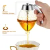A hand is holding a honey dispenser over a cup, demonstrating how it dispenses honey. Produktbild-Vorschau