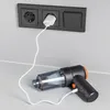 A black and orange handheld vacuum cleaner is plugged into a wall socket via a white USB cable, charging. Produktbild-Vorschau