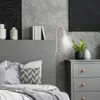 A bedroom setting with a bed, dresser, and wall lamp. Náhled obrázku produktu