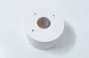 A white circular mounting bracket with a central hole and three smaller holes on the top surface, placed on a white surface. Produktbild-Vorschau