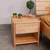 A wooden nightstand with decorative items on top, next to a bed. Produktbild-Vorschau