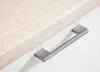 A close-up view of a cabinet handle on a white surface, next to a marble countertop. Náhled obrázku produktu