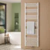 A white towel radiator is mounted on a light brown wall in a bathroom. A white towel is draped over one of the bars. In the background, a white bathtub and a small wooden stool are visible. Produktbild-Vorschau