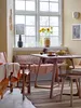 A cozy dining area with a wooden table and chairs, a bench by the window, and decorative items. Produktbild-Vorschau