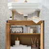 A bathroom vanity cabinet with a sink above it, showcasing storage and decorative items. Náhľad obrázku produktu