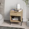 A bedside table with a lamp, books, and glasses on it, next to a bed. Produktbild-Vorschau